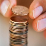 Fingers Holding Penny Above Stack of Pennies